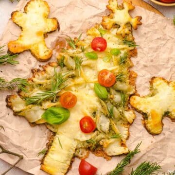 A Christmas tree-shaped cheesy bread with tomatoes, basil, and herbs, on parchment paper, with breadstick figures.