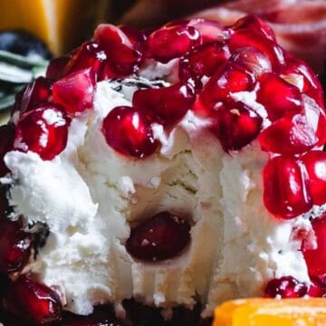 A ball of soft cheese topped with pomegranate seeds, with a bite taken out of the center.