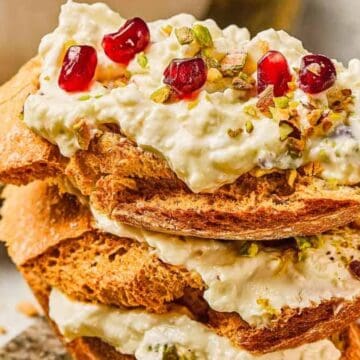 Toasted bread slices topped with creamy cheese, pomegranate seeds, and chopped pistachios.