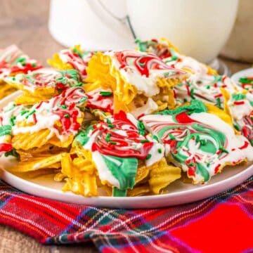 Wavy chips coated in white chocolate with red and green swirls on a plate, on a plaid cloth.