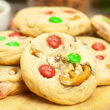 Thick cookies with red and green chocolate candies and pretzel pieces on a wooden board.