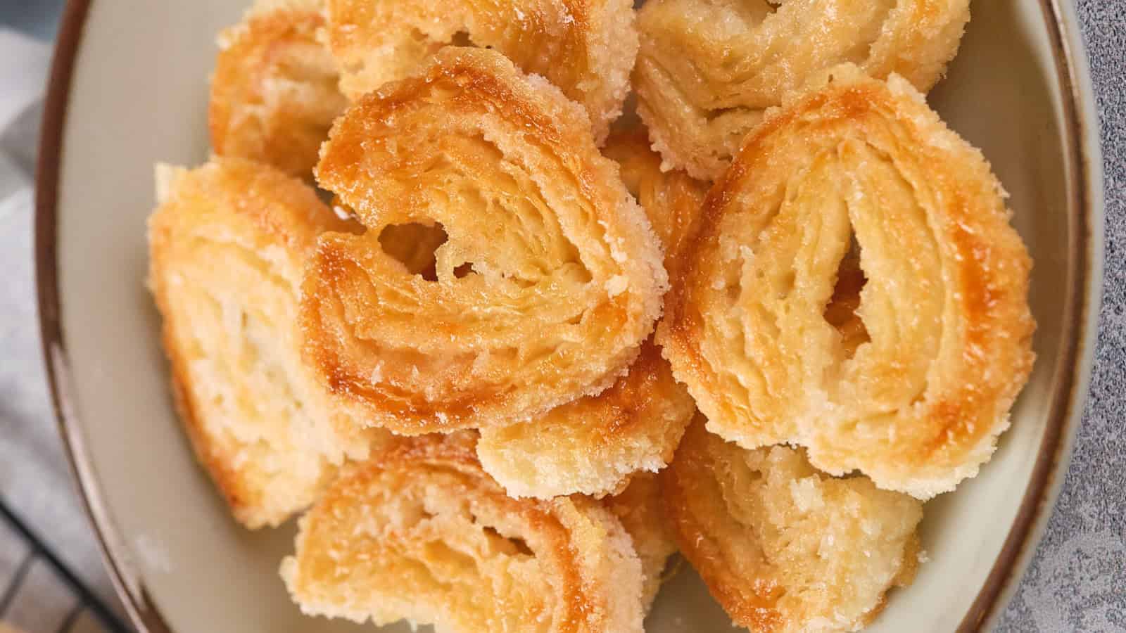 A plate of golden, heart-shaped puff pastry palmiers with a sugar coating.