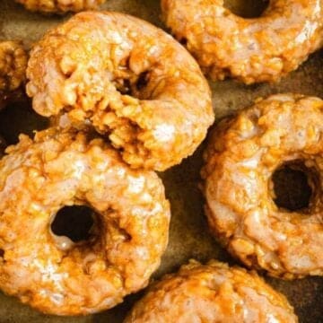 Glazed donuts with a crunchy texture arranged closely together on a dark baking sheet.