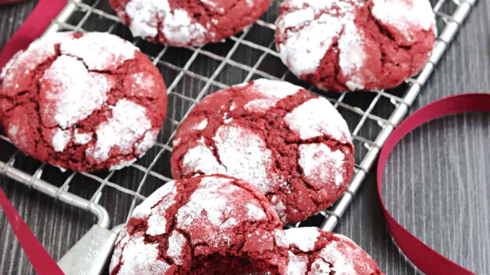 Red crinkle cookies dusted with powdered sugar on a cooling rack, with a red ribbon beside them.
