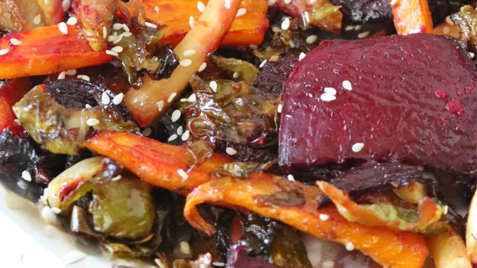 Close-up of roasted vegetables, including carrots and beets, sprinkled with white sesame seeds.