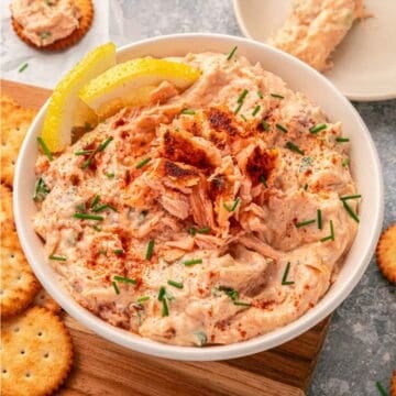 Bowl of Salmon Dip garnished with chives and lemon slices, served with crackers on the side.
