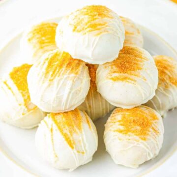 A plate of white chocolate-coated dessert balls topped with golden cookie crumbs, stacked in a pyramid.
