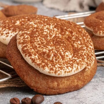 Cookies topped with swirled frosting and cocoa powder, cooling on a wire rack with coffee beans nearby.