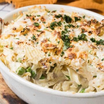 A baked casserole topped with crispy onions and herbs in a white dish on a wooden board.
