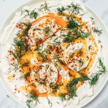 Whipped yogurt topped with poached eggs, paprika oil, and fresh dill on a white plate.