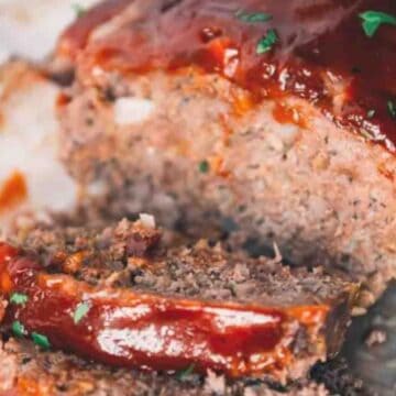 Sliced meatloaf topped with ketchup glaze, garnished with chopped parsley on parchment paper.