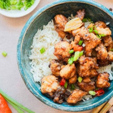 A bowl of white rice topped with stir-fried chicken pieces and chopped green onions, with chopsticks beside it.