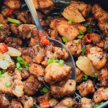 Close-up of cooked, seasoned chicken pieces with sliced chili, garlic, and green onions in a pot with a spoon.