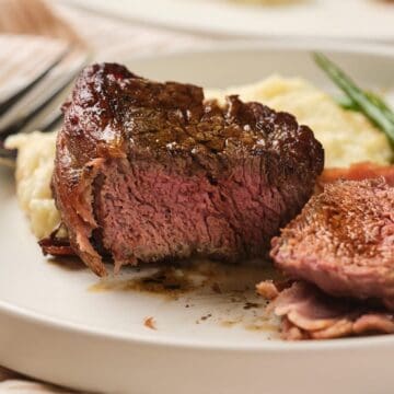 A plate with steak, mashed potatoes, and green beans, with a knife and fork beside the food.