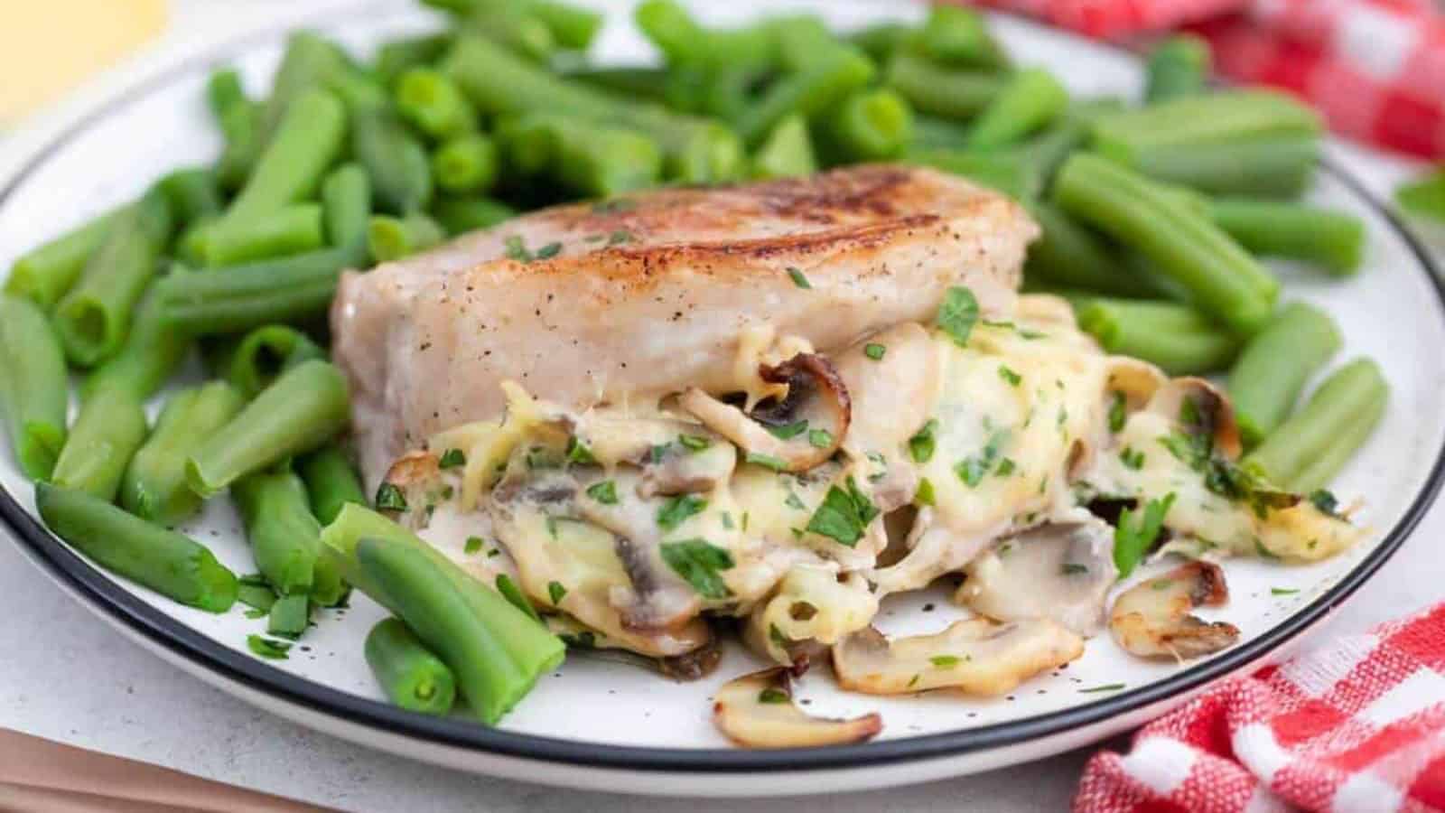 A plate of pork chops stuffed with mushrooms and cheese served with green beans.