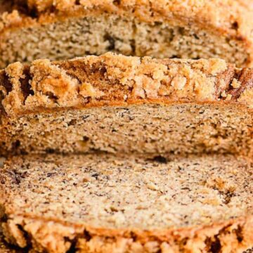 Sliced banana bread with a crumbly topping on a wooden cutting board.