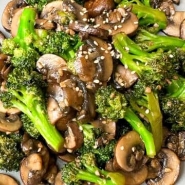 Stir-fried broccoli and mushrooms topped with sesame seeds on a gray plate, with chopsticks beside them.