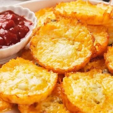 A plate of crispy baked cheese rounds with a small bowl of red dipping sauce on the side.