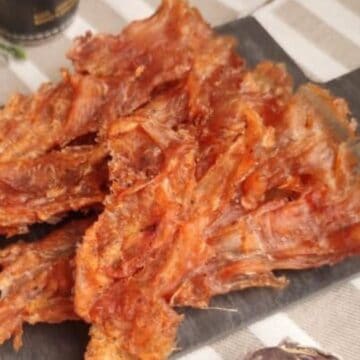 Several pieces of dried, crispy fish are arranged on a black rectangular plate on a striped tablecloth.