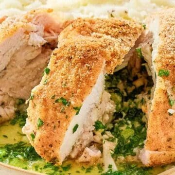 Breaded chicken breast sliced open, revealing a herbed buttery filling, served with mashed potatoes.