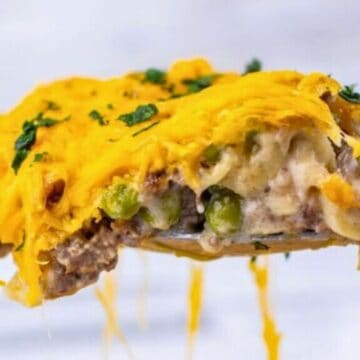 A spoonful of cheesy shepherd’s pie with ground meat, peas, and melted cheddar, garnished with parsley.