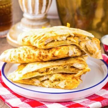 Three pieces of stuffed flatbread stacked on a plate, on a red checkered cloth, with sauce on the side.