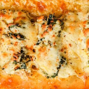Baked cheesy spinach and chicken casserole in a glass dish, topped with melted golden-brown cheese.