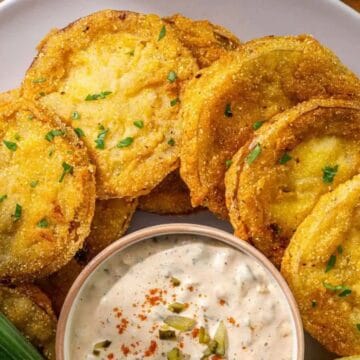 A plate of fried green tomatoes garnished with herbs, served with a side of creamy dipping sauce.