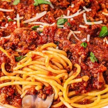 A plate of spaghetti topped with chunky meat sauce and garnished with grated cheese and parsley.