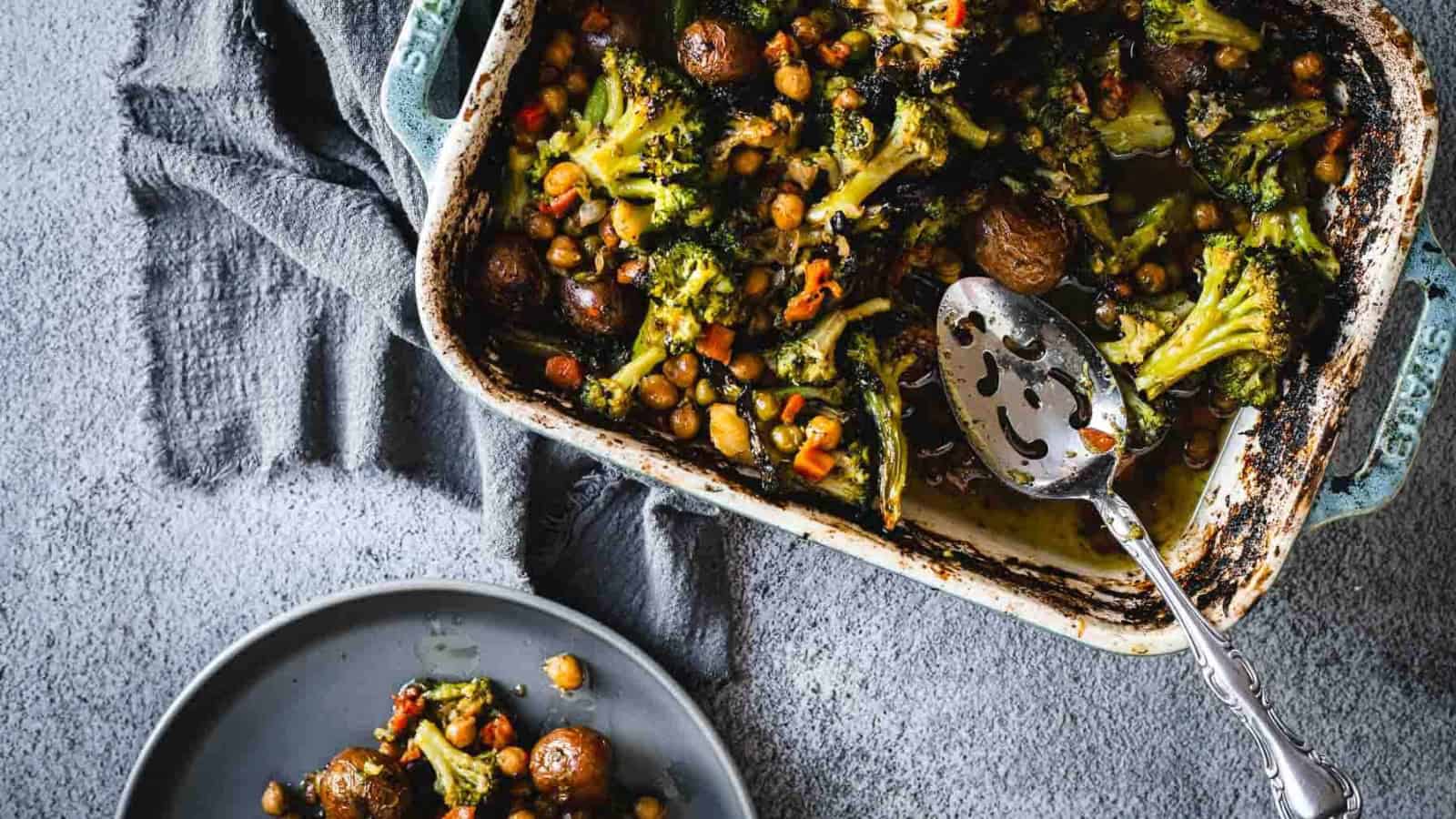 A casserole dish filled with roasted broccoli, potatoes, chickpeas, and diced vegetables.