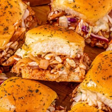 Several barbecue chicken sliders with coleslaw on golden buns are arranged on a wooden surface.