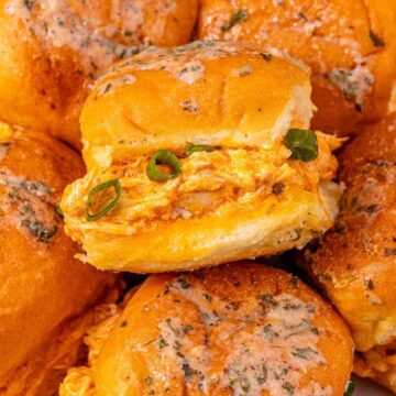 Close-up of stuffed bread rolls with herbs, spices, and green onions on a white plate.