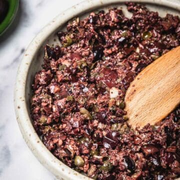 A bowl of Easy Olive Tapenade being mixed with a wooden spoon.