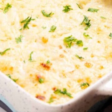 Baked cheesy casserole topped with melted cheese and sprinkled with chopped parsley in a white dish.
