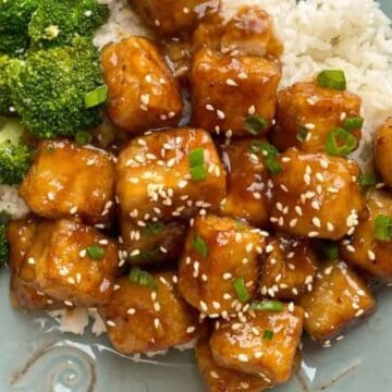 A plate with white rice, broccoli, and sesame-topped glazed tofu cubes garnished with green onions.