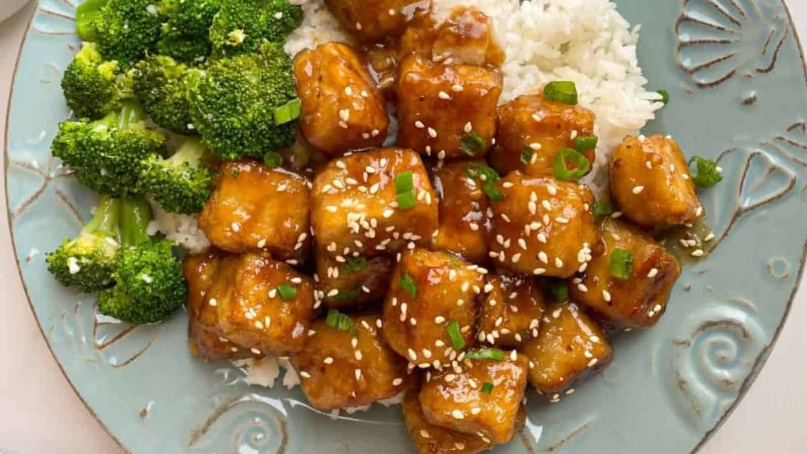 Glazed tofu cubes with sesame seeds and chives on rice, accompanied by steamed broccoli.