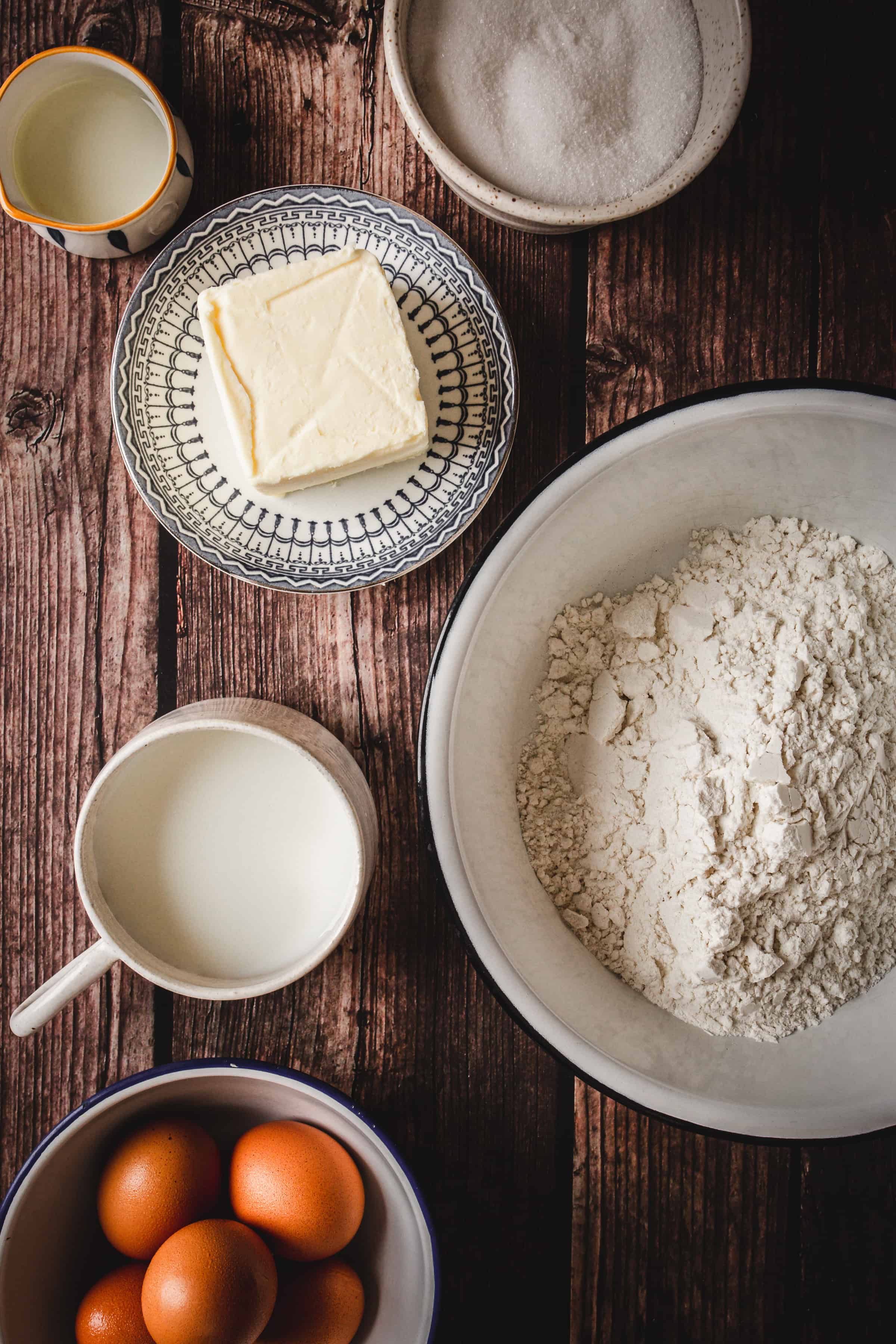 Baking ingredients on a table: flour, butter, sugar, milk, and eggs in separate bowls and cups&mdash;perfect for making traditional Russian rolled wafers.