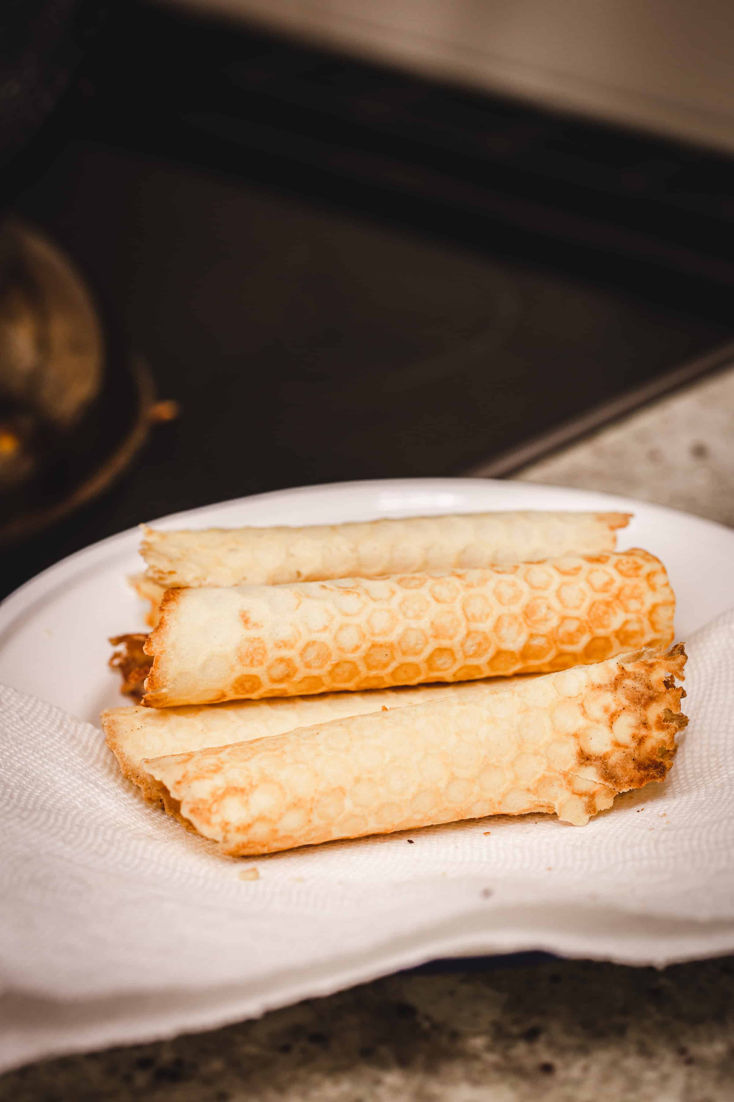 Three traditional Russian rolled wafers rest on a white plate lined with a paper towel, set on a kitchen countertop.