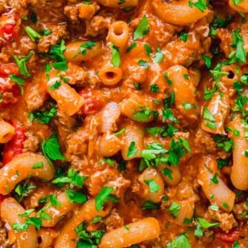 Close-up of macaroni pasta with ground beef, tomato sauce, and chopped parsley on top.