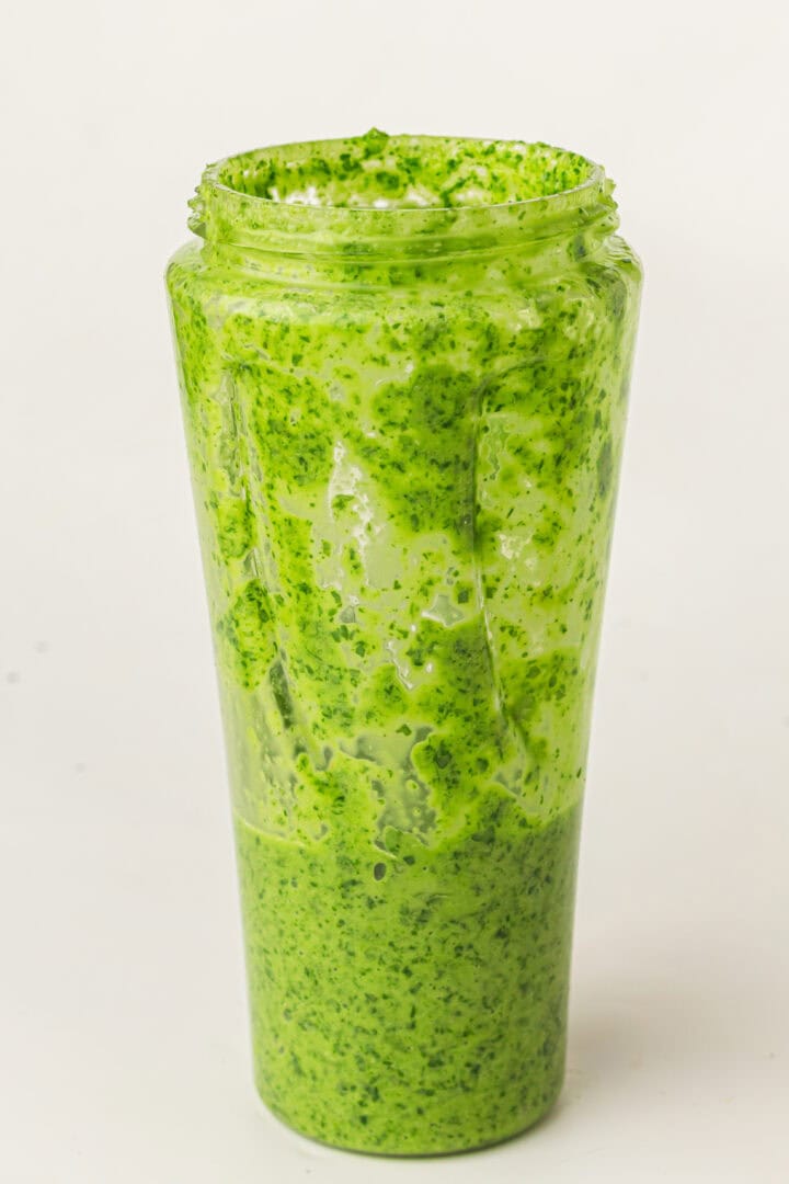 A tall glass filled with creamy green sauce, with some sauce smeared on the inside of the glass.