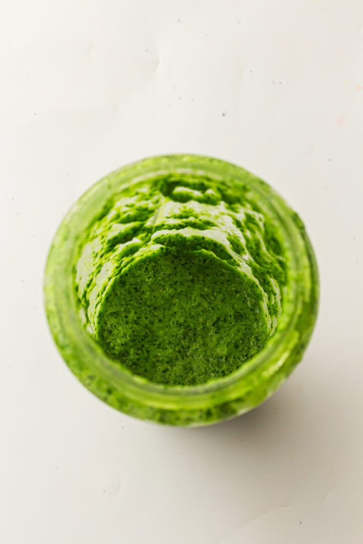 Open jar filled with bright green pesto sauce viewed from above on a white background.