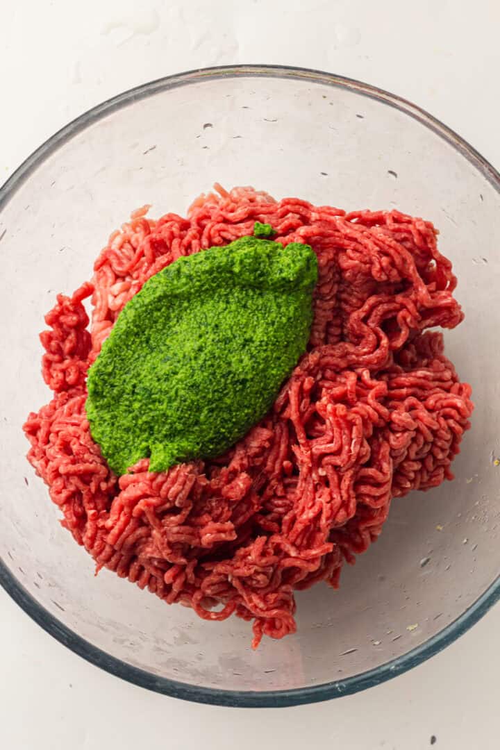 Ground beef in a glass bowl with a mound of bright green herb paste on top.