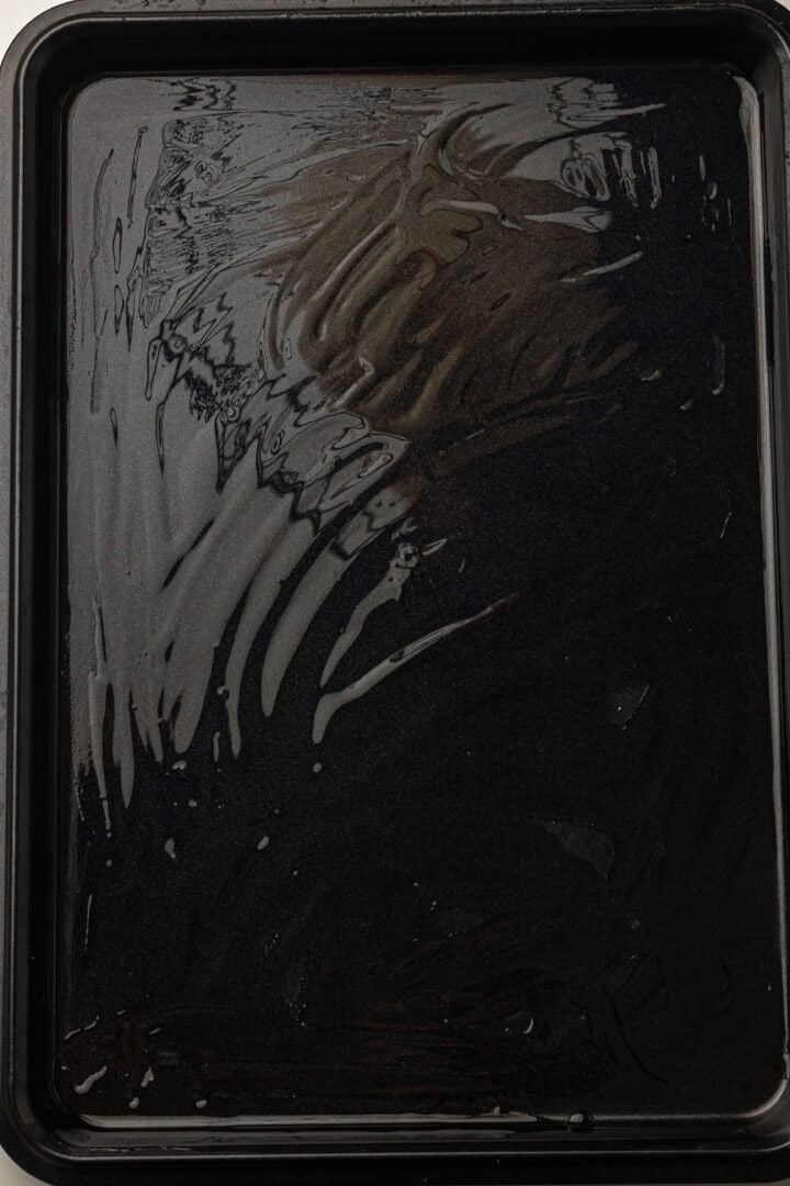 A black baking tray coated with a thin layer of oil, ready for use.