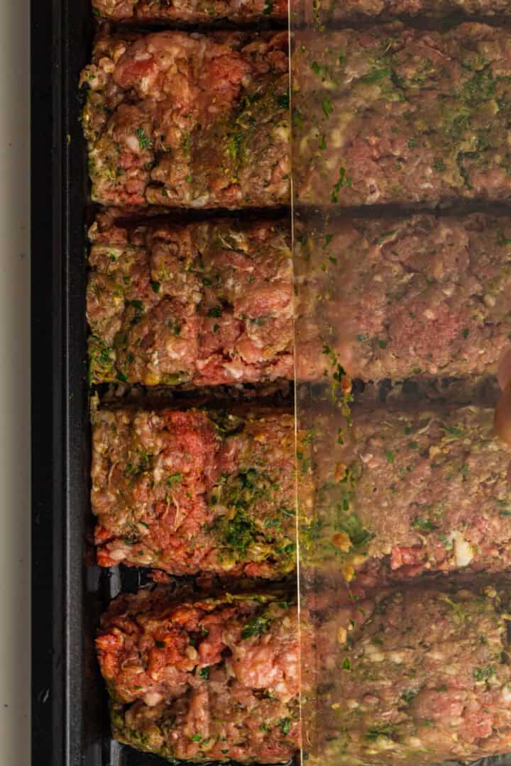 Raw seasoned ground meat divided into rectangular portions on a tray, about to be covered with plastic wrap.