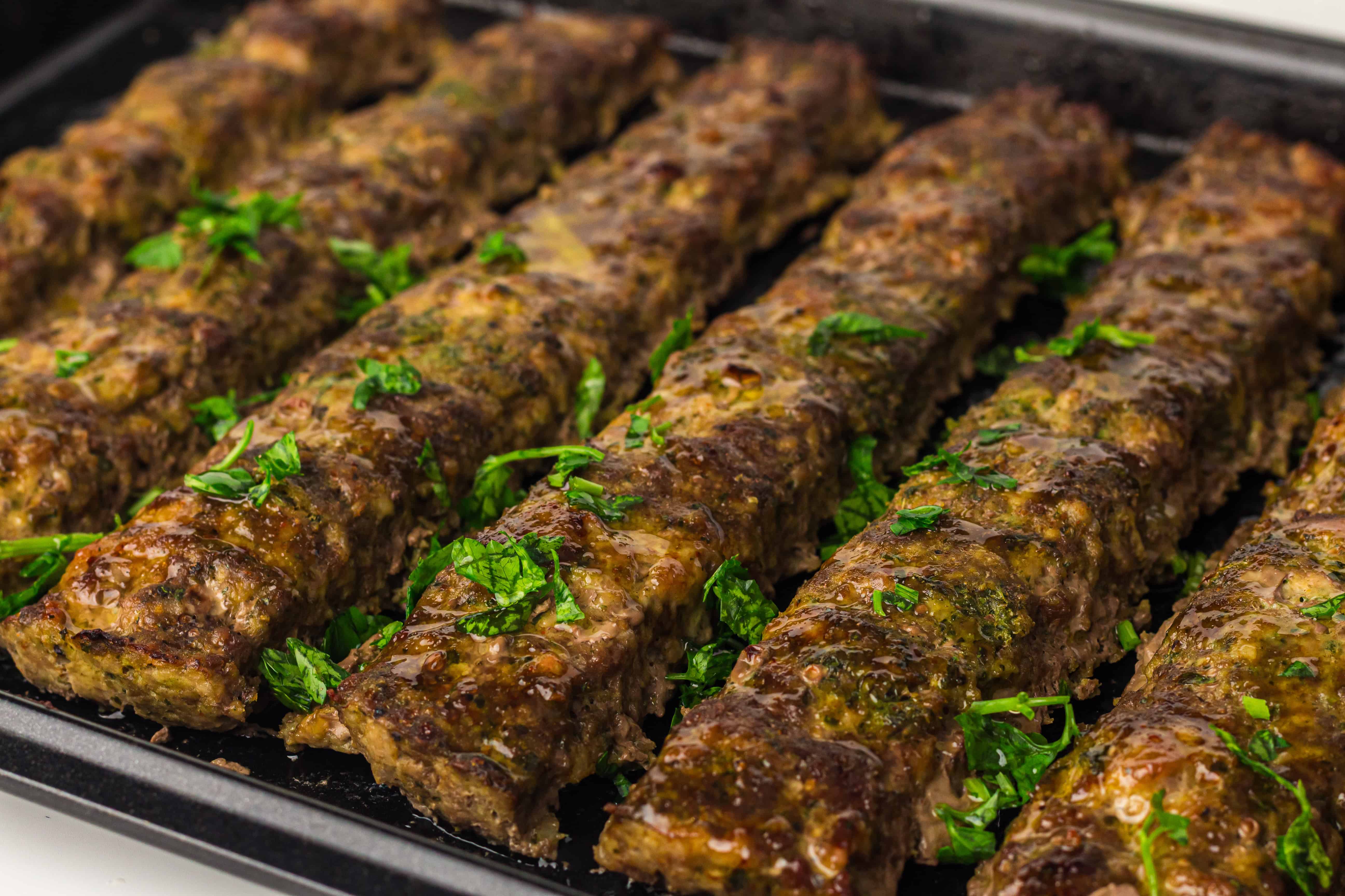 Rows of grilled kebabs garnished with chopped parsley, arranged neatly on a dark tray.