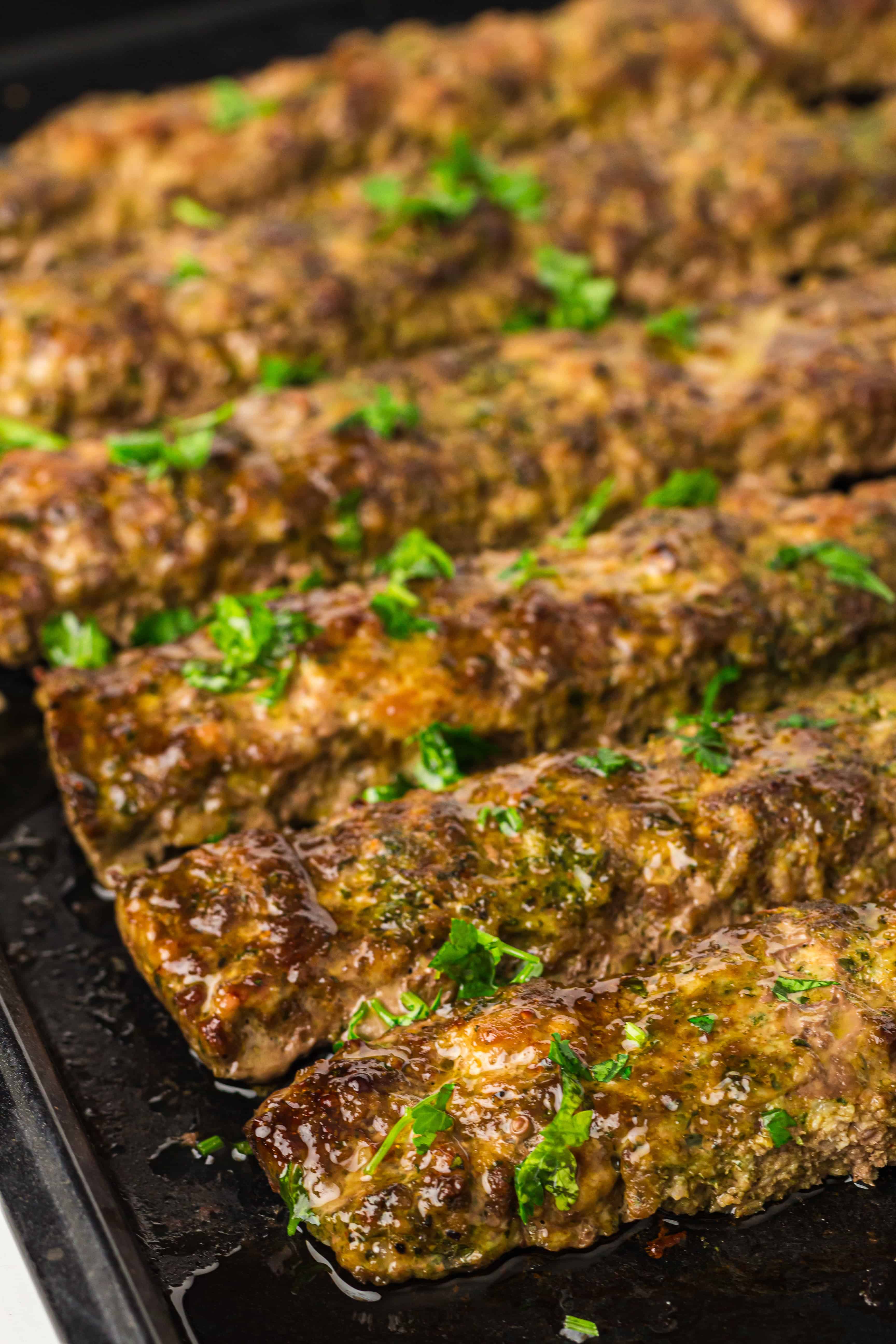 Grilled kebabs garnished with chopped parsley on a black tray.
