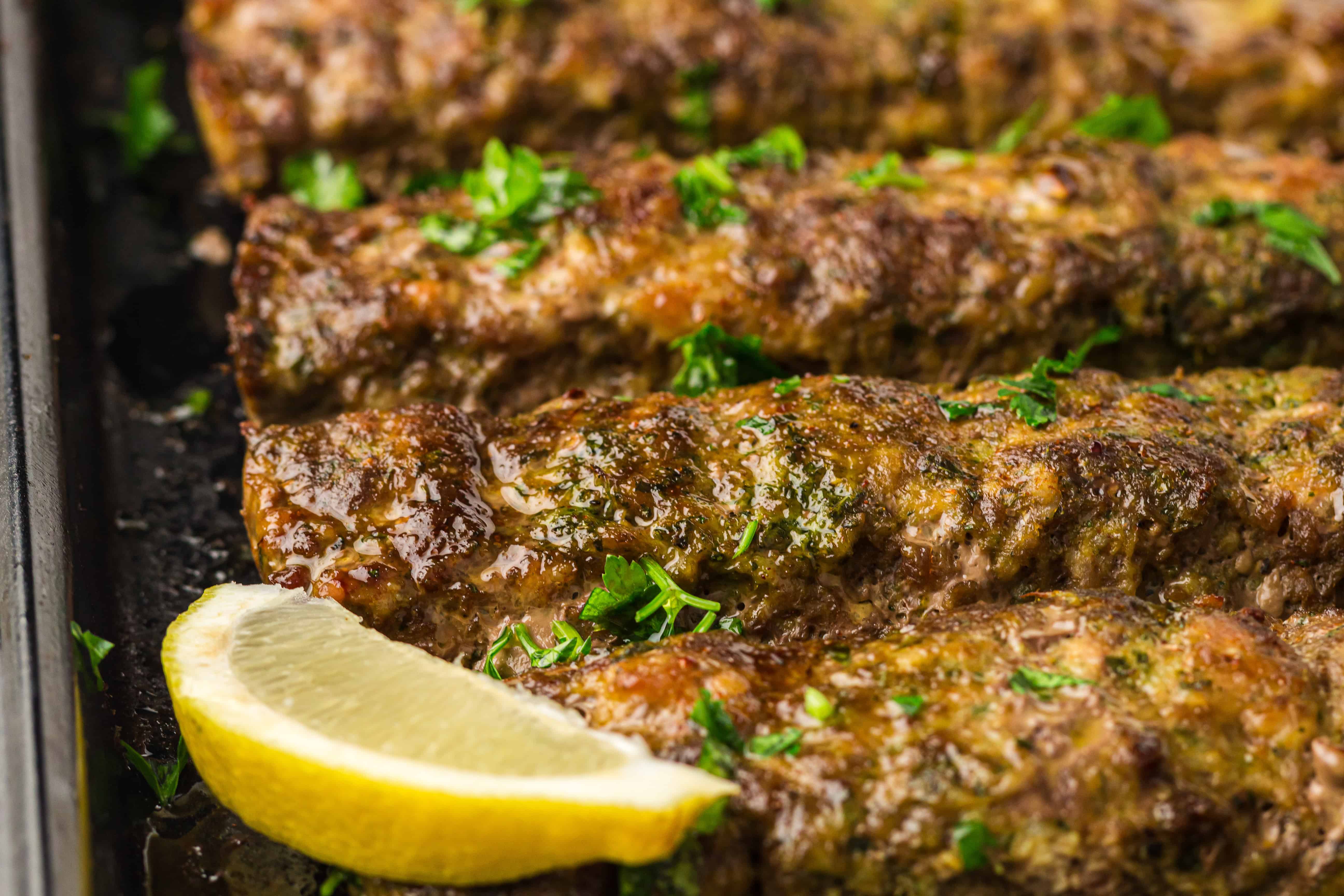Close-up of grilled kebabs garnished with chopped herbs, with a lemon wedge on the side.