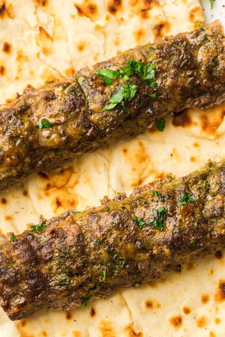 Two grilled kebabs topped with herbs on flatbread.