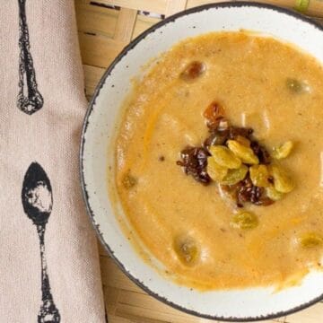 A bowl of creamy dessert garnished with golden raisins, placed on a tray beside a printed napkin.