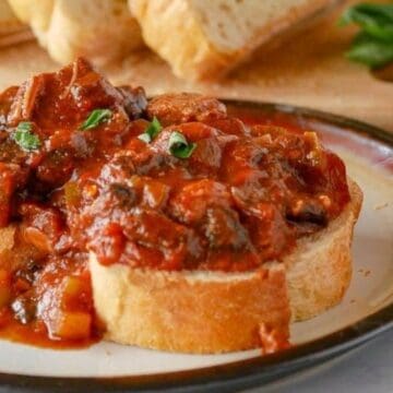 Two slices of bread topped with chunky tomato and vegetable stew on a plate, bread loaf in background—a hearty nod to forgotten recipes from kitchens past.